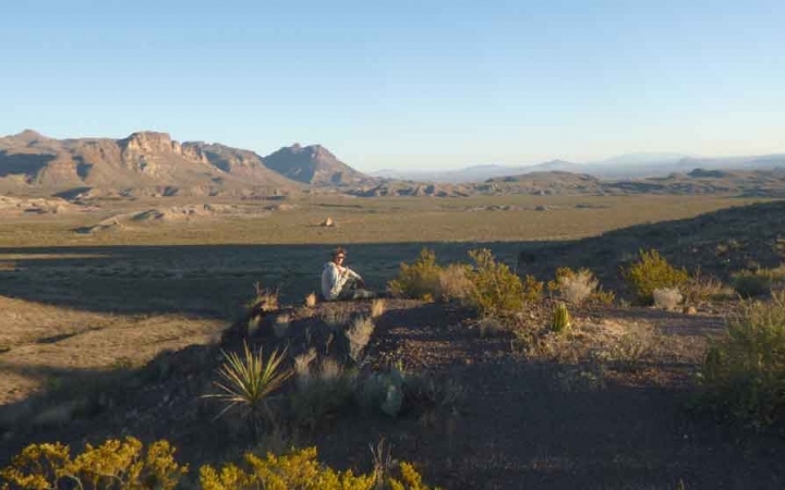 a gap year student sits on an elevated position, overlooking a desert landscape with a mountain in the background